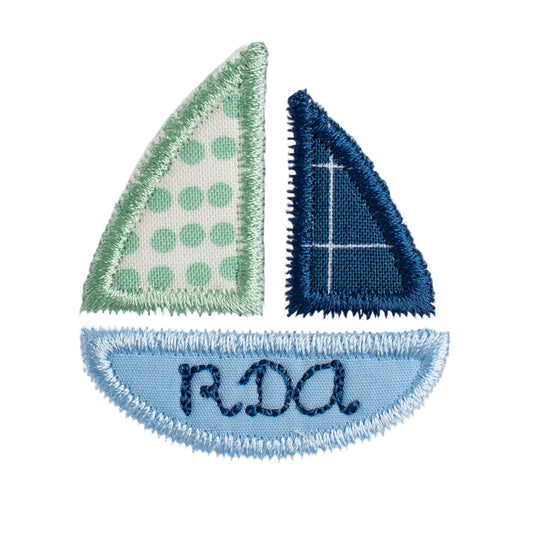 Close up of Deacon Lane's signature sailboat applique design for boys. The bottom of the boat is personalized with embroidered monogram