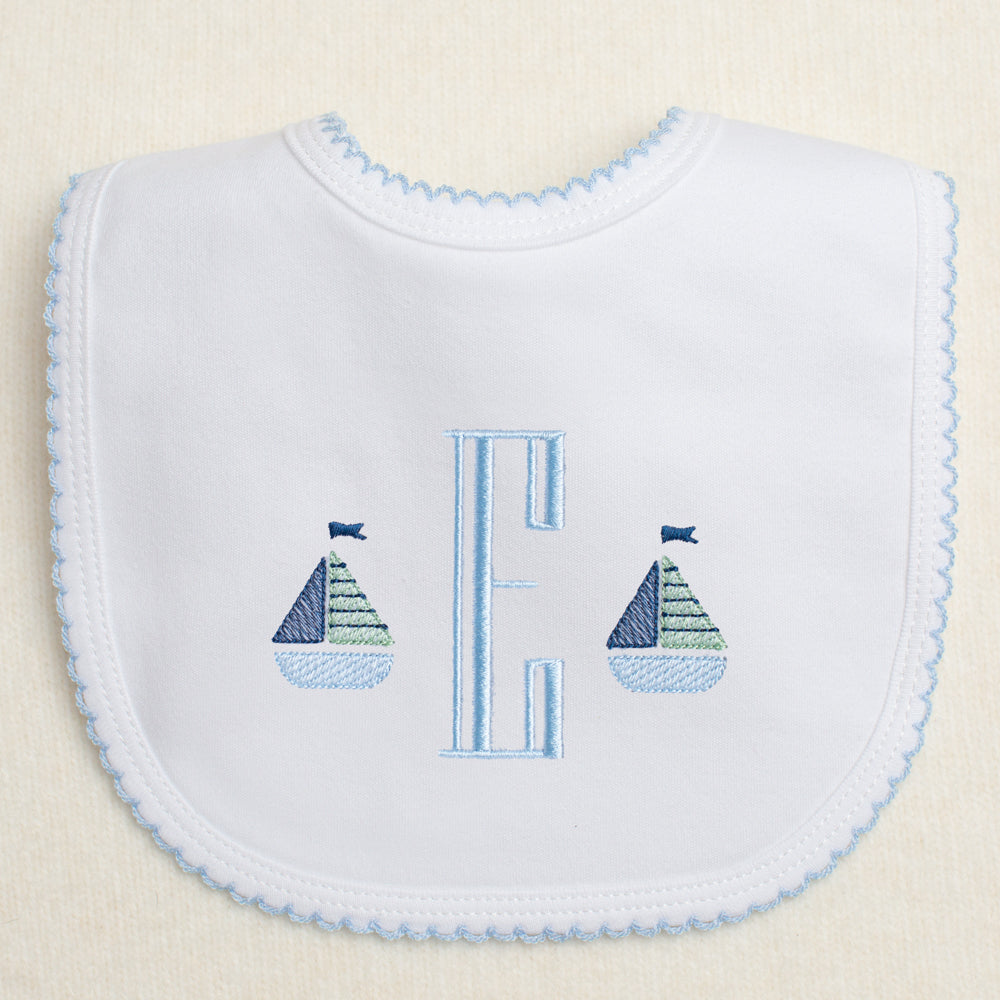 white knit cotton bib with blue picot trim featuring a monogram with two mini sailboats embroidered on either side.