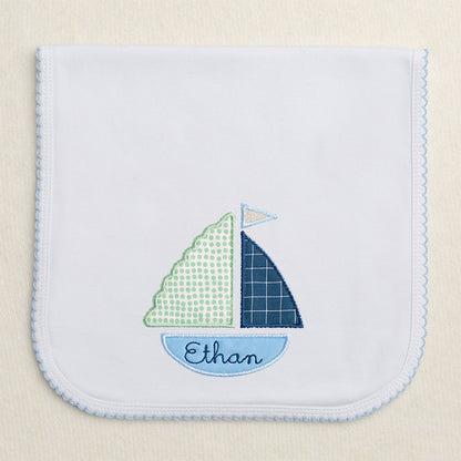 Blue picot trimmed burp pad with blue and green applique sailboat with embroidered name in the hull of the boat.