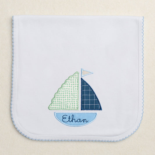 Blue picot trimmed burp pad with blue and green applique sailboat with embroidered name in the hull of the boat.