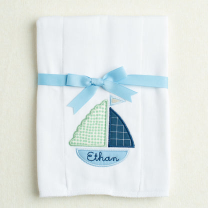White burp pad with sailboat design and blue ribbon on a beige background