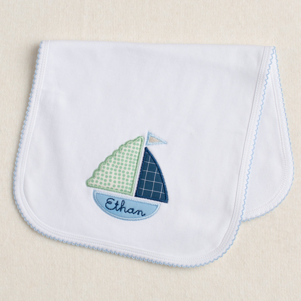 White knit burp pad with blue picot edging featuring an appliqued boat that has custom embroidery in the bottom of the boat.  One of a kind personalized gift.
