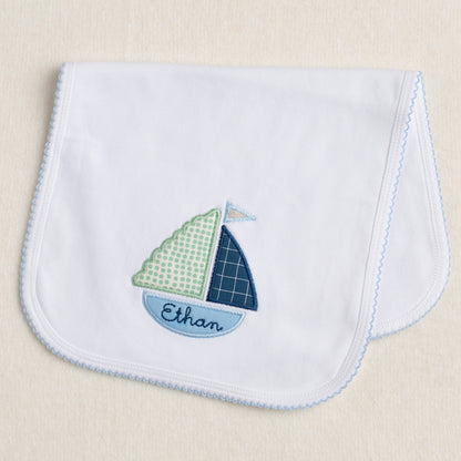 White knit burp pad with blue picot edging featuring an appliqued boat that has custom embroidery in the bottom of the boat.  One of a kind personalized gift.
