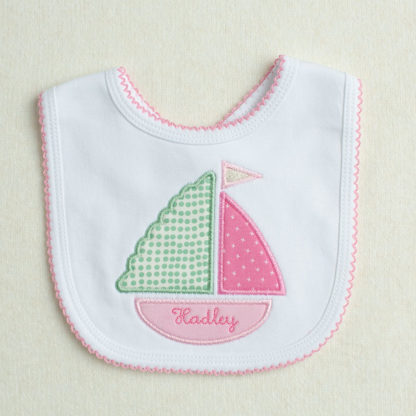 Cotton baby bib with pink applique sailboat in graphic fabrics in shades of pink, green, and cream