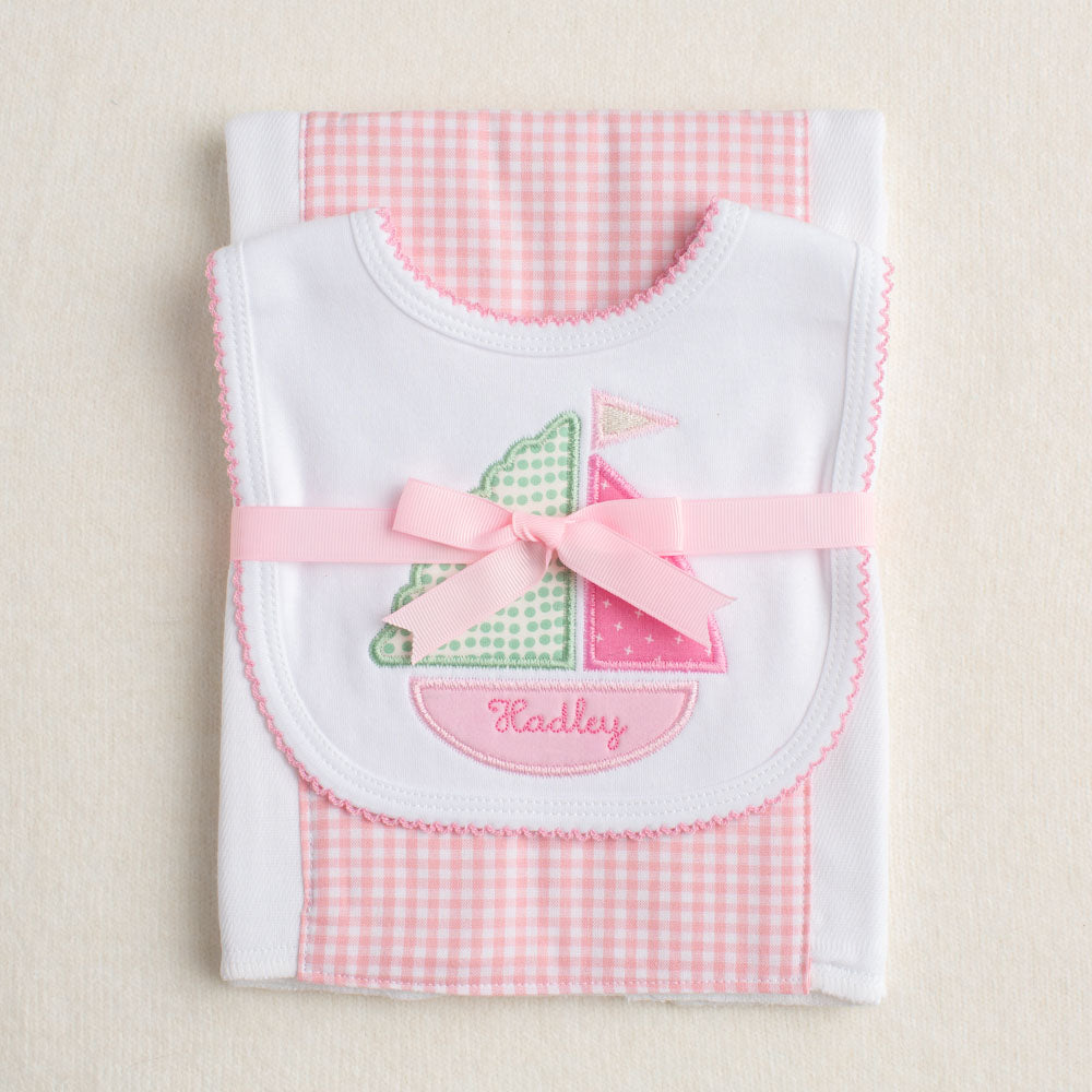Two piece packaged gift set with a sailboat bib and a pink check burp cloth