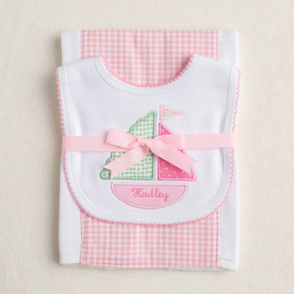 Two piece packaged gift set with a sailboat bib and a pink check burp cloth