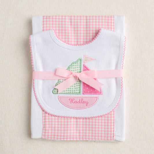 Two piece packaged gift set with a sailboat bib and a pink check burp cloth