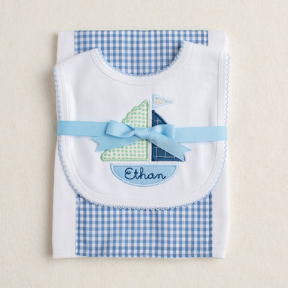 Handmade 2 piece gift set presented ready for gift giving folded and tied with a grosgrain ribbon.  Set includes blue check fabric burp pad along with a white bib with Deacon Lane's appliqued sailboat motif with a name custom embroidered in the bottom of the boat.