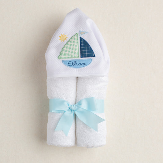 white hooded towel rolled and tied with a beautiful grosgrain ribbon.  Hood on towel comes embellished with Deacon Lane's exclusive sailboat applique design with carefully curated fabrics and an extra special custom embroidery of the child's name inside the bottom of the boat.