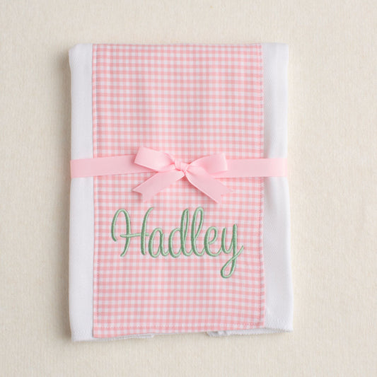 Pink gingham personalized burp pad with a bow and 'Hadley' monogram on a beige background