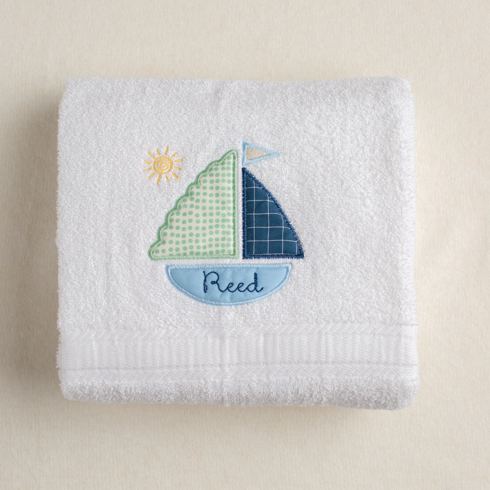 All white bath towel with a jaunty sailboat applique in Deacon Lane's exclusive Sailboat design featuring a custom embroidered name inside the bottom of the boat.