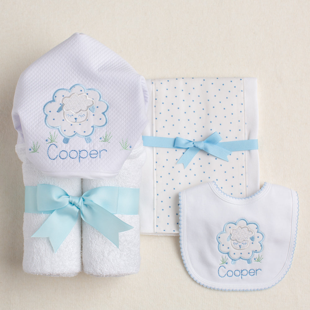 3 piece boutique baby set featuring Deacon Lane's Blue Fluffy Sheep collection with a hooded towel, fabric burp pad, and bib with picot trim.  2 of the items are personalized with a child's name embroider on the item.