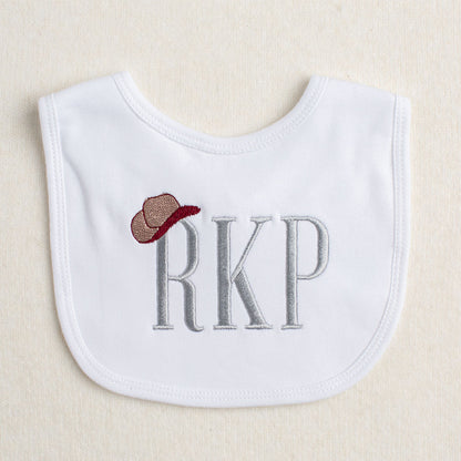 white bib with a monogram with a cowboy hat hanging on one letter