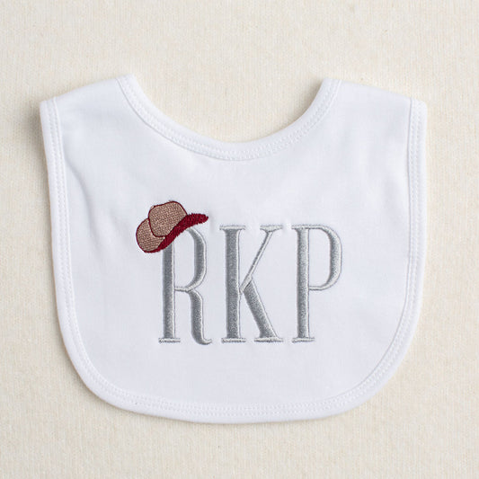 white bib with a monogram with a cowboy hat hanging on one letter