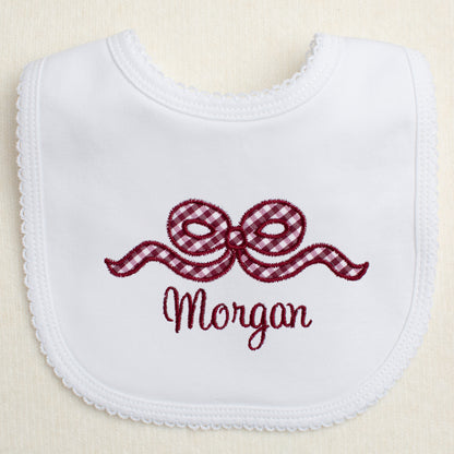 white bib with a picot edge with an appliqued maroon bow and a personalized, embroidered name for Texas A + M fans