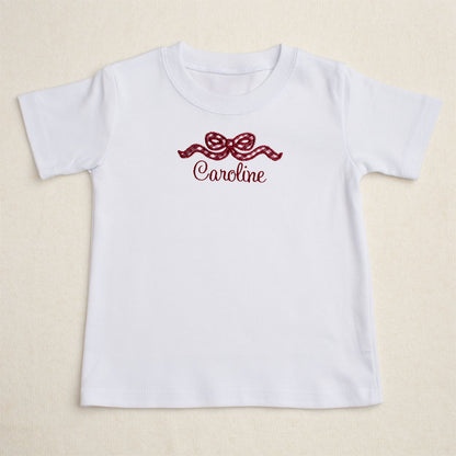 White t-shirt with a maroon check applique bow with a personalized name for Aggie fans.