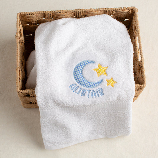 White towel with embroidered moon and star design in a wicker basket on a beige background