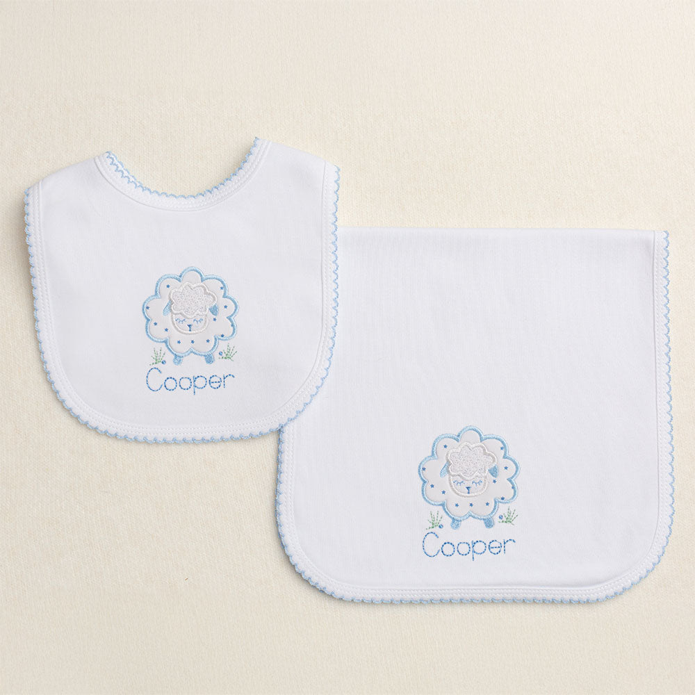 Baby gift set of two white knit items with a blue picot edge - a burp pad and a bib.  Features Deacon Lane's Blue Fluffy Sheep applique with a personalized name
