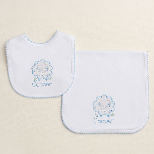 Baby gift set of two white knit items with a blue picot edge - a burp pad and a bib.  Features Deacon Lane's Blue Fluffy Sheep applique with a personalized name
