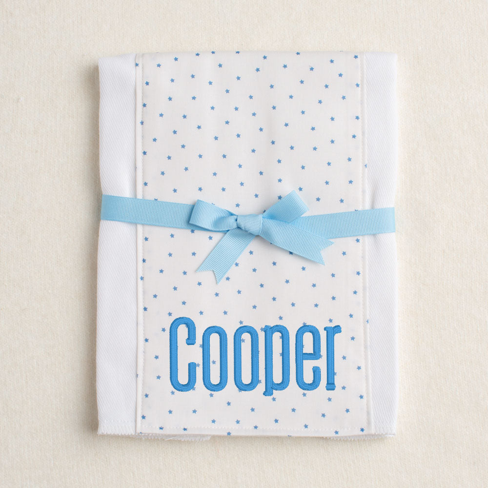Boutique baby burp pad with blue star fabric panel sewn down the center.  Personalized with embroidery and packaged tied with a grosgrain bow.