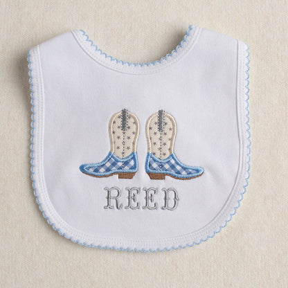 All cotton baby bib with blue picot trim with a cowboy boot embroidered applique in light blue, cream, and grey. Personalized with a name in a western fishtail font.