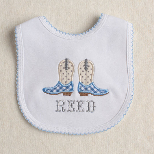 All cotton baby bib with blue picot trim with a cowboy boot embroidered applique in light blue, cream, and grey. Personalized with a name in a western fishtail font.