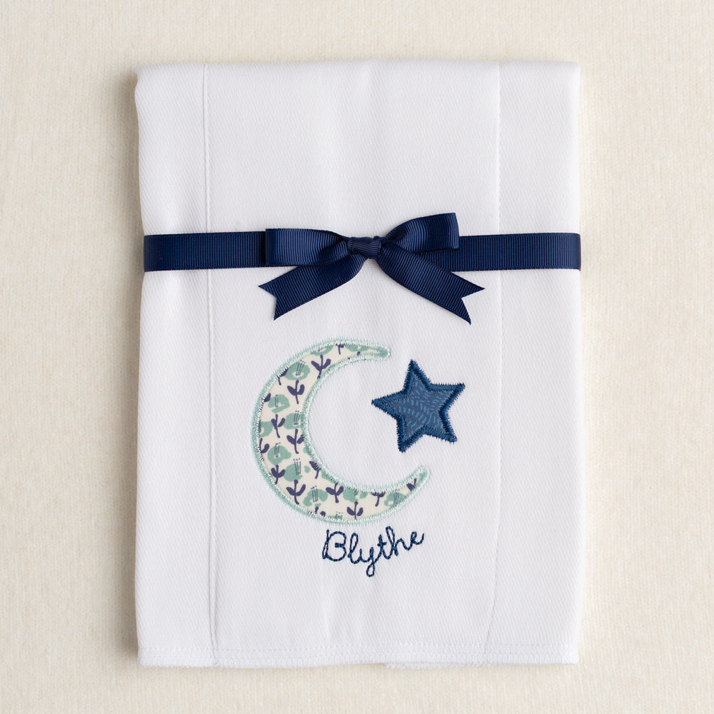 Cloth diaper burp pad with a navy and seafoam fabric in a moon and star applique with a personalized embroidered name hugging the moon.