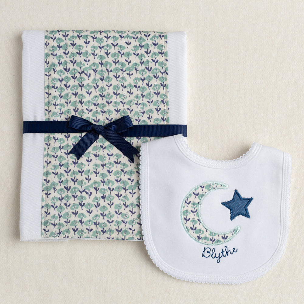 Boutique baby gift set of a burp pad with a fabric panel down the center and a bib appliqued with a moon and star motif made of fabric reminiscent of a Liberty print