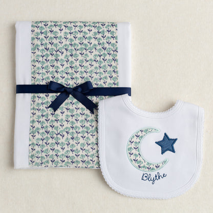 Boutique baby gift set of a burp pad with a fabric panel down the center and a bib appliqued with a moon and star motif made of fabric reminiscent of a Liberty print