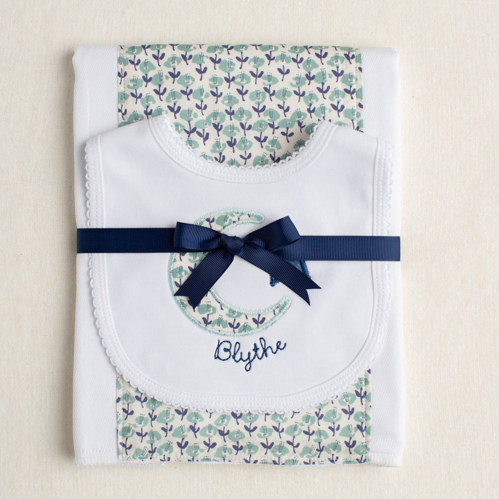 Boutique baby gift set of a burp pad with a fabric panel down the center and a bib appliqued with a moon and star motif made of fabric reminiscent of a Liberty print