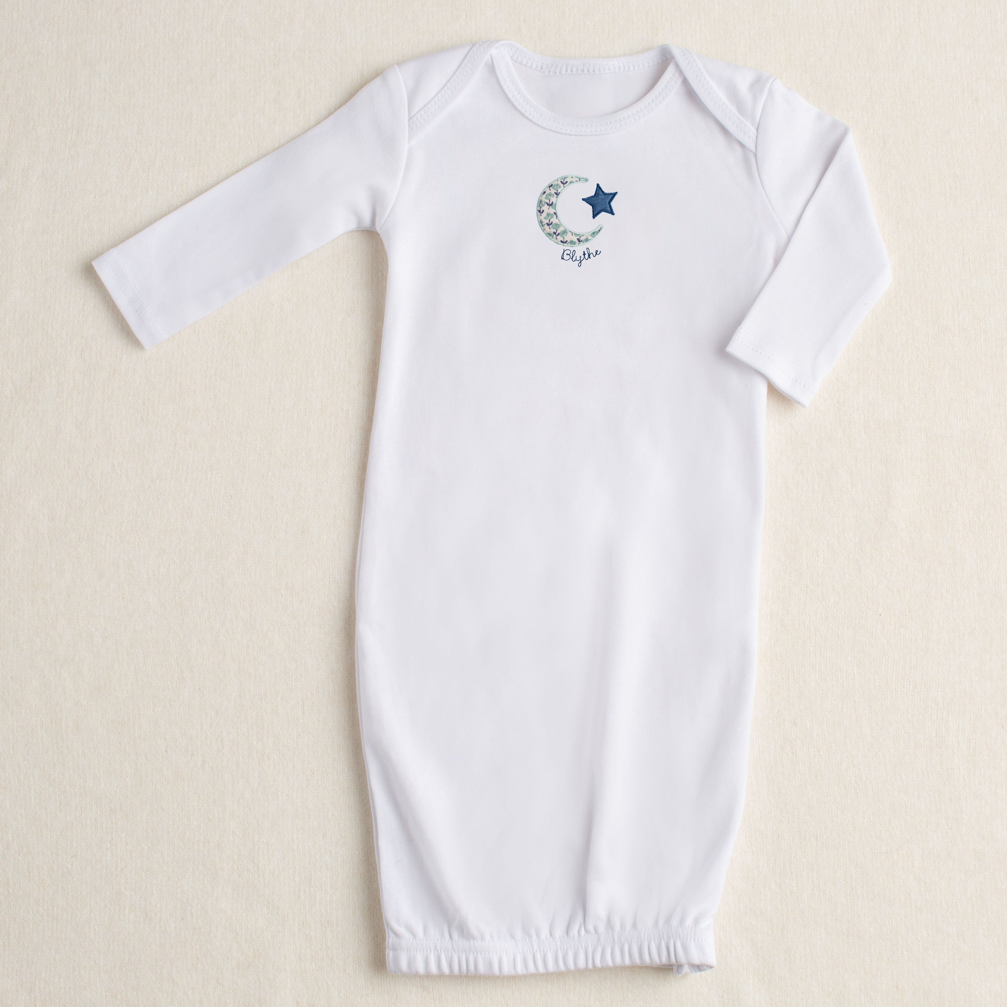 White baby gown with Deacon Lane's Bella Notte applique design in a navy/seafoam floral.