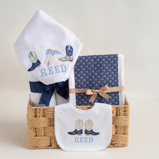Personalized baby gift set with appliqued hooded towel, burp pad with a navy fabric panel, and a bib with appliqued cowboy boots
