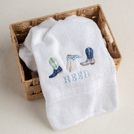White bath towel with a trio of appliqued cowboy boots with a name embroidered in a western fishtail font.