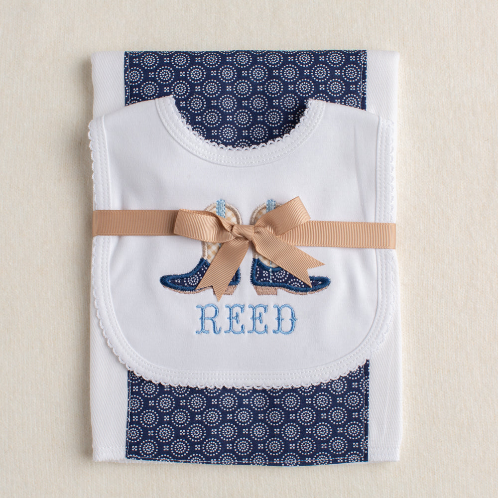 2 piece set gift ready with a cowboy motif of appliqued cowboy boots on a white bib pair with a fabric burp pad with a western theme navy fabric panel down the middle.