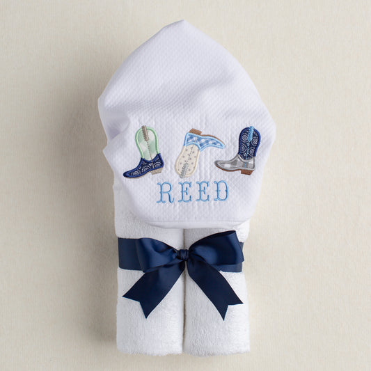 white terry hooded towel with appliqued and personalized hood featuring a trio of three appliqued cowboy boots in shades of navy, baby blue, sage, and grey