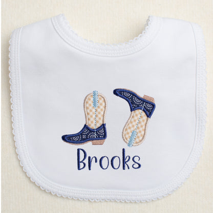 personalized hand made white cotton knit bib with picot trim with a pair of appliqued cowboy boots and a personalized name in shades of navy, light blue, and khaki