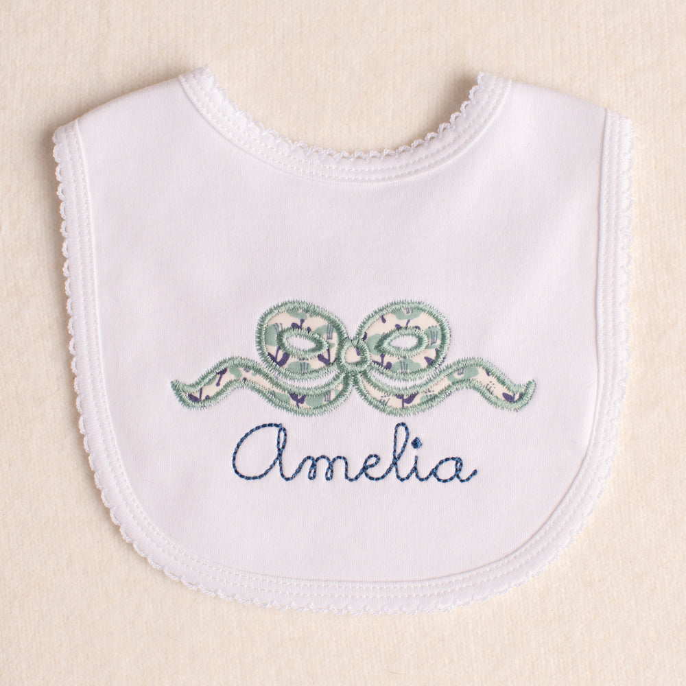 white picot trimmed bib with Deacon Lane's signature bow applique in a navy and sage/seafoam floral print