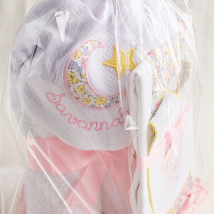 Packaged personalized boutique baby gift of a hooded towel, a fabric burp pad and an appliqued bib with a picot edge.  Personalized gift giving with a nod to Liberty of London 