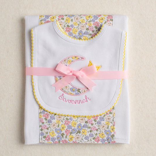 Boutique baby gift set with a pink floral fabric burp pad paired with a cotton bib with a picot trimmed edge and a hand appliqued moon and star motif made from a pink floral fabric that is reminiscent of a Liberty of London fabric.
