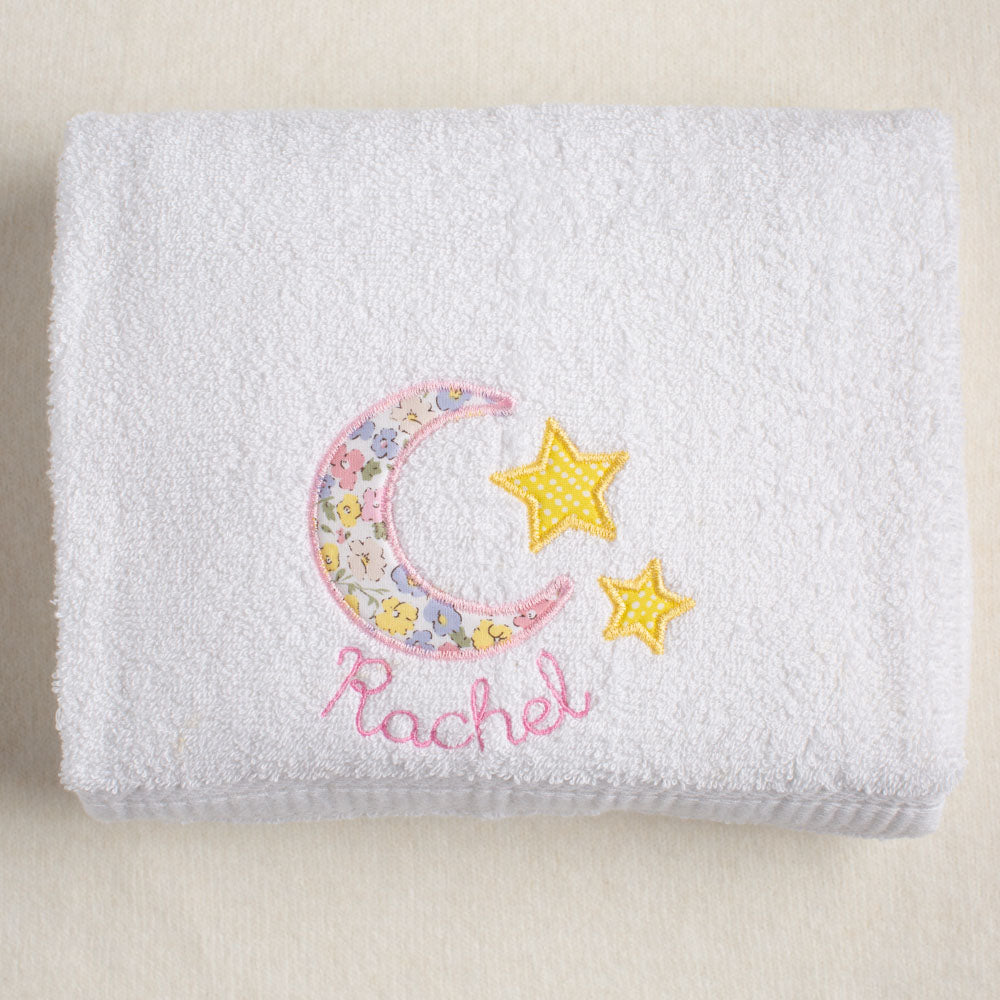 White towel with floral moon and stars design and embroidered name 'Rachel' on a beige background
