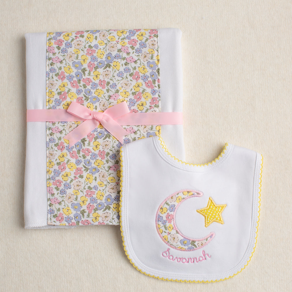 Close up view of a baby baby gift set of a fabric burp pad and an appliqued bib featuring a pink floral fabric reminiscent of a Liberty of London fabric.

