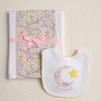 Close up view of a baby baby gift set of a fabric burp pad and an appliqued bib featuring a pink floral fabric reminiscent of a Liberty of London fabric.
