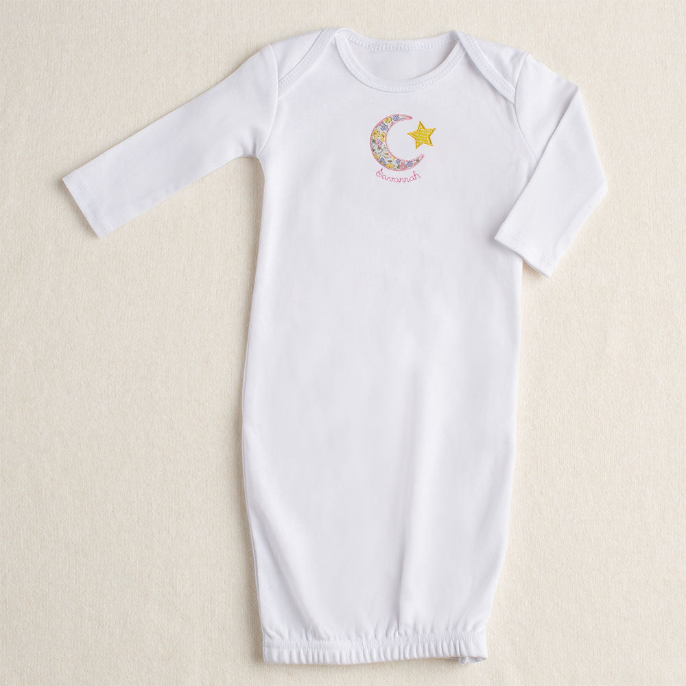 A white cotton gown in NB - 3 Months that features a zipper closure at the bottom and sports a handmade applique motif made from a Liberty of London like floral print in pink, yellow, and lavender.