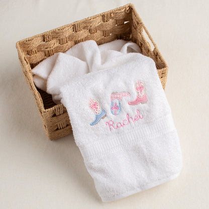 White towel with embroidered text and boot designs in a woven basket on a light background