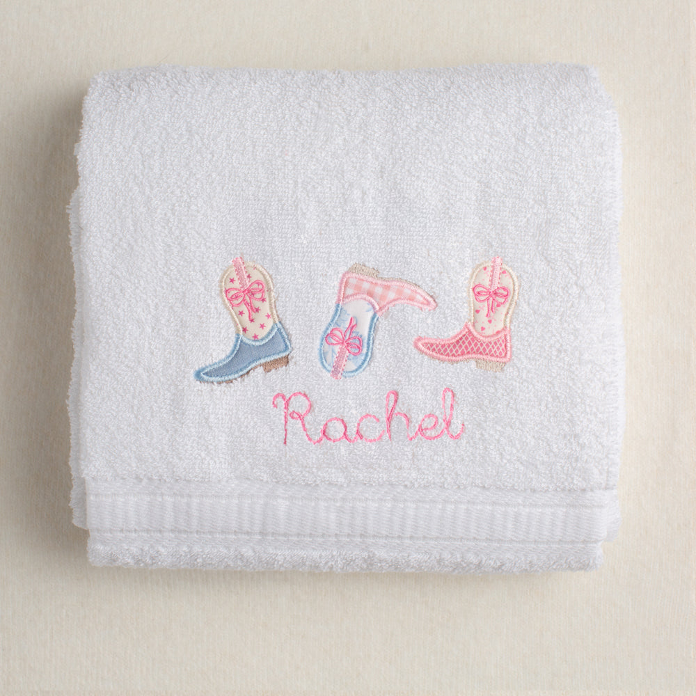 Folded towel with embroidered boot designs and the name 'Rachel'.