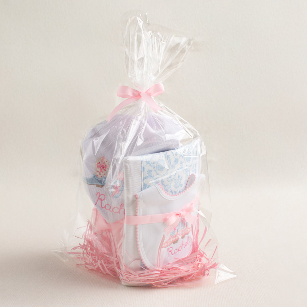 Personalized baby gift set with a Shabby Chic Cowgirl motif featuring appliqued cowboy boots in pink check and blue toile.  Includes a hooded towel, a fabric burp pad, and a personalized bib.  Wrapped in clear cello for easy gift giving.