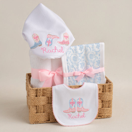 Personalized baby gift set with a Shabby Chic Cowgirl motif featuring appliqued cowboy boots in pink check and blue toile.  Includes a hooded towel, a fabric burp pad, and a personalized bib.