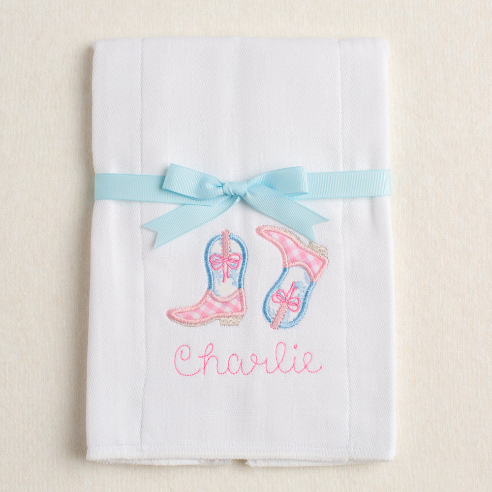 Personalized burp pad with appliqued cowboy/cowgirl boots in a pink check and and blue floral toile.  Packaged folded and tied with a grosgrain ribbon