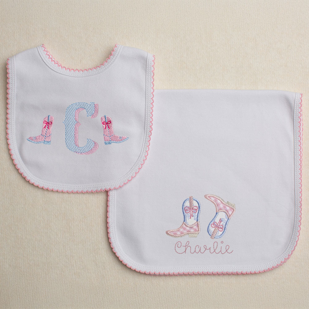 Monogrammed cotton bib with pink picot trim featuring a western theme font with cowboy boots with bows.  Set includes a personalized burp pad with pink picot trim with appliqued cowboy boots