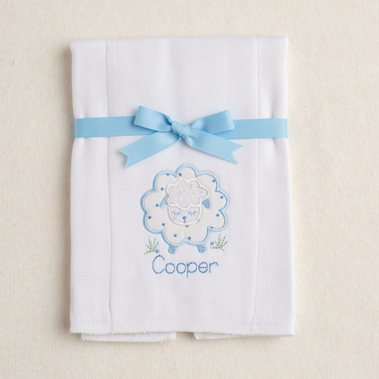 White burp pad with blue embroidered sheep packaged and tied with a bow